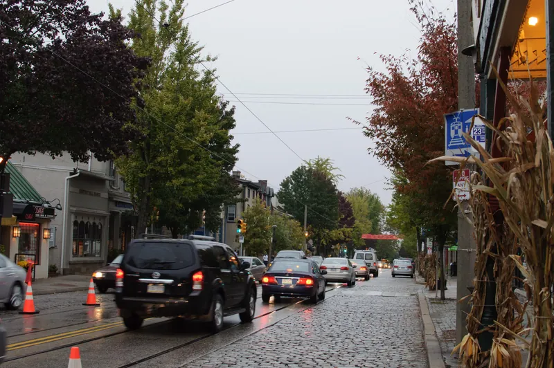 Cobblestone Germantown Avenue lined with shops and autumn trees